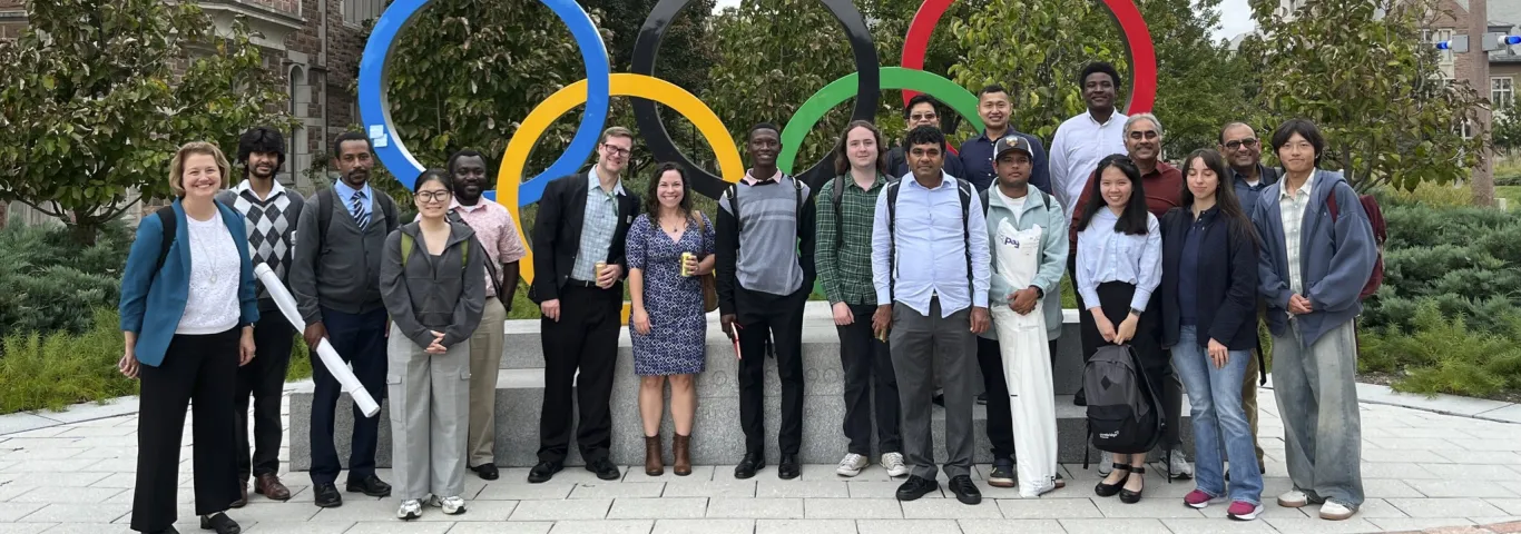 Nineteen attendees of ASA Day 2026 pose in front of the Olympic rings on WashU's Danforth Campus