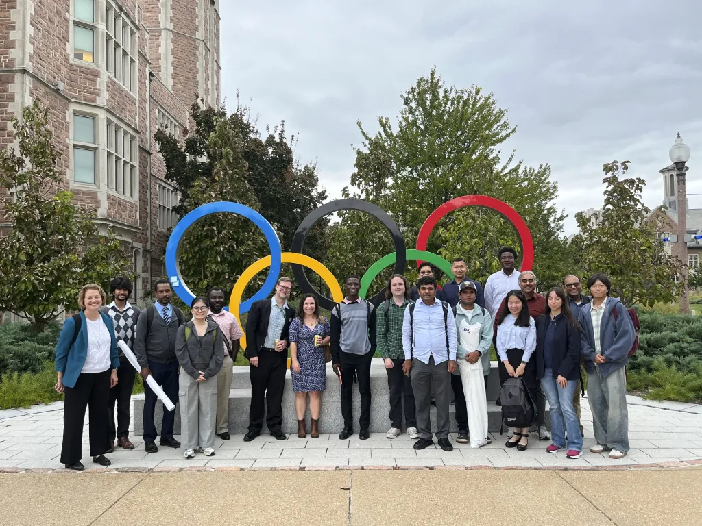Nineteen attendees of ASA Day 2026 pose in front of the Olympic rings on WashU's Danforth Campus