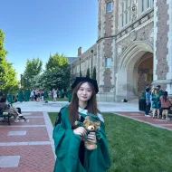 Luyi Zhang smiles for the camera on the WashU campus, wearing her graduation robes